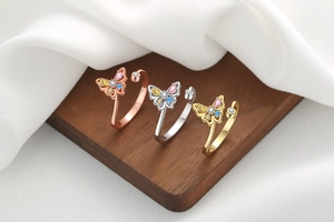 Close-up of gold and silver hollow butterfly rings with colorful cubic zirconia on wood