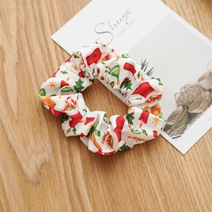 Detailed view of white fabric Christmas scrunchie with festive hat and gift patterns
