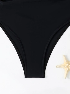 Detail view of high-cut black bikini bottoms with starfish decor on white textured background