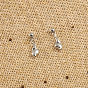 Détail de boucles d'oreilles boules en acier argenté avec pendentif coquillage sur tissu