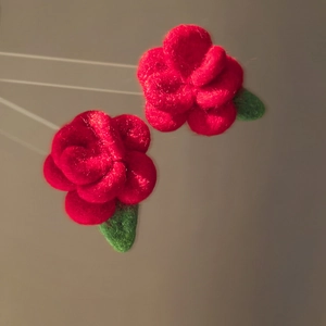 Close-up of red flocked rose flower earrings with green leaves and silver pins