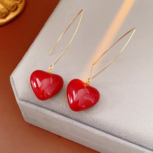 Detail of vintage gold hook earrings with glossy red heart-shaped pendant on gray stand