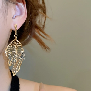 Close-up of gold hollow leaf earrings with 3D butterfly detail on model ear