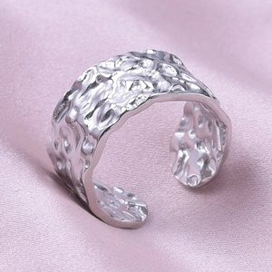 Detail of silver hammer-textured stainless steel ring on soft pink silk fabric background