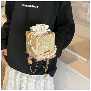 Detail of woven straw handbag featuring faux pearl handle and gold chain strap close-up