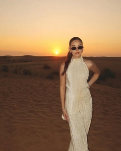 Detail of elegant pleated halter neck dress in beige shown against a desert sunset backdrop