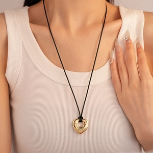 Close-up of a gold geometric heart pendant on a black cord necklace worn by a model