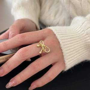 Detailed close-up of a golden bow ring worn with a soft white knitted sweater background