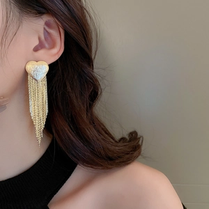 Close-up of golden heart tassel earrings with long metallic fringe chains on model