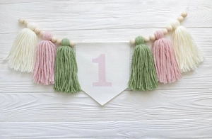 Detail of baby first birthday high chair banner with pink number 1 and colorful tassels