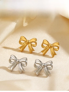 Detail of gold and silver bow stud earrings on cream silk with matte finish texture