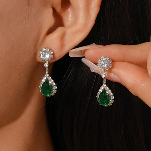 Close-up of emerald teardrop earrings with silver setting on model, luxury jewelry detail