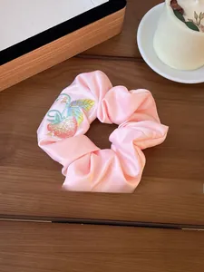 Detailed embroidery of strawberries on a soft pink satin scrunchie on dark wood