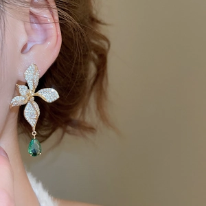 Macro view of flower-shaped earrings with 18k gold plating and green teardrop gemstone