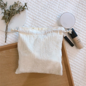 Macro detail of creamy white lace drawstring pouch with floral embroidery on wood tray