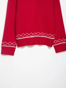 Détail d'un pull en maille rouge avec broderie losange blanche et ourlet côtelé