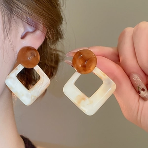 Macro shot of marble textured geometric resin earrings with amber beads on ear