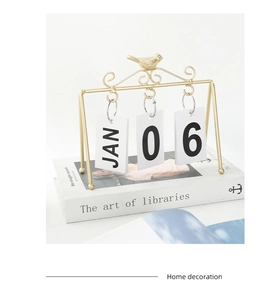 Detail of golden metal bird flip calendar with artistic scroll stand and date cards