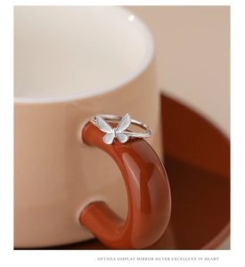 Detailed macro shot of a silver butterfly ring hanging on a ceramic cup handle