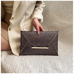 Détail d'une pochette enveloppe marron pailletée avec boucle dorée sur tissu beige