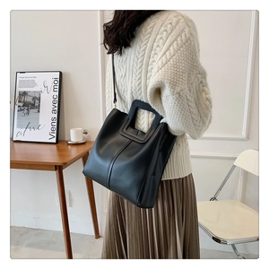 Detail of the elegant black matte leather bucket bag paired with a beige knit outfit