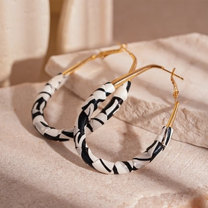 Detail of gold hoop earrings with black and white woven texture on a stone surface
