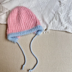 Close-up of pink and blue contrast knit winter hat with plush mohair texture and ear flaps