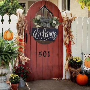 Close-up of wooden welcome door sign with white flowers and striped bow on a red door