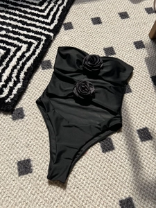 Detail view of 3D rose flower embellishments on a black cutout one-piece swimsuit