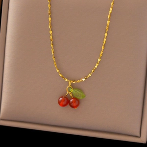 Detailed shot of golden cherry necklace with red fruit and green leaf in beige jewelry box