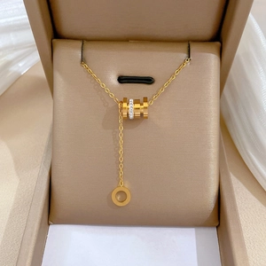 Collier en acier titane doré avec pendentif cylindre orné de cristaux dans un écrin