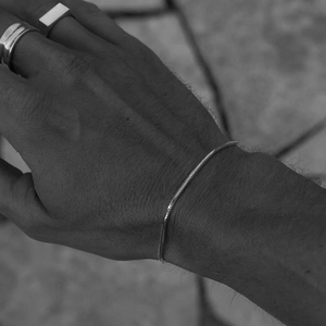 Detail of silver snake bone chain bracelet worn by male with minimalist metal rings