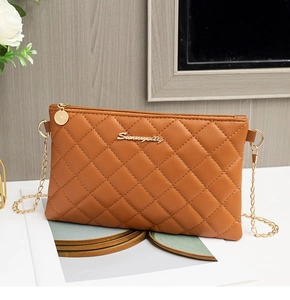 Détail du sac enveloppe matelassé caramel avec chaîne dorée et logo métallique