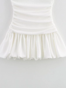 Detailed close-up of white dress with smocked waist texture and ruffled hemline details