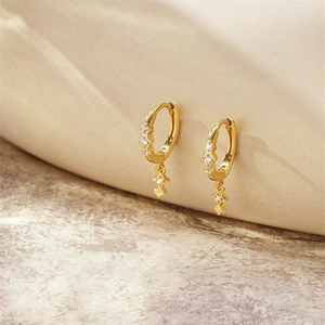 Détail de boucles d'oreilles créoles dorées avec zircons et pendentifs étoile sur céramique