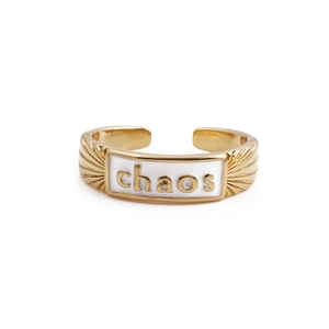 Dettaglio dell'anello regolabile dorato con smalto bianco e scritta chaos decorativa