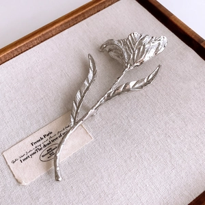 Close-up of a silver tulip brooch with a polished mirror finish on linen tray