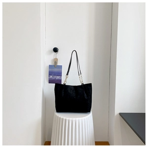 Detail of black matte tote bag with slim shoulder straps and gold metal chain accents