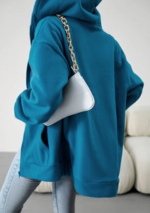 Back view of a loose teal fleece hooded sweatshirt paired with a white faux leather bag
