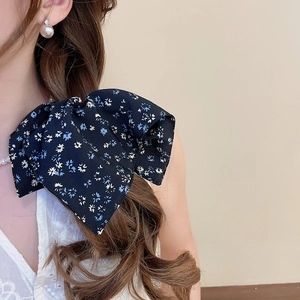 Detail of a large navy floral bow hair tie with white and blue patterns on model's hair