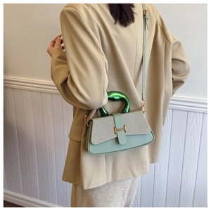 Detail of light green contrast handbag with metallic wavy handle and golden H-clasp