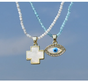 Dettaglio della collana di perline con ciondolo malocchio e croce su sfondo cielo blu