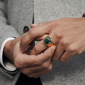 Detailed close-up of a men's gold signet ring with a deep green gemstone inlay