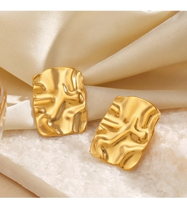 Macro detail of 18K gold plated rectangular earrings with hammered texture on white stone