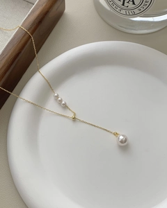 Detailed view of s925 gold tassel necklace featuring white pearls on a ceramic dish