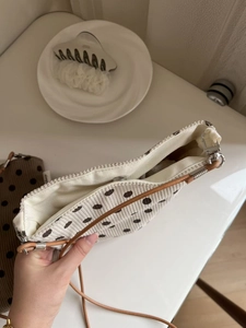 Close-up of beige polka dot corduroy bag with magnetic closure and brown strap