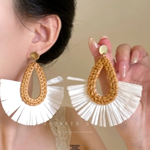 Detail of bohemian raffia drop earrings featuring woven straw and white fringe on model