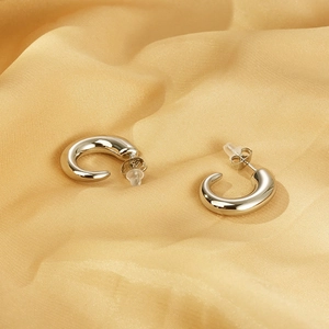 Macro detail of silver C-shaped earrings on gold silk with butterfly backings