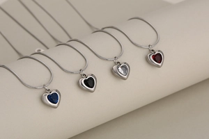 Close-up of four minimalist heart pendant necklaces with crystals in colorful snake chains