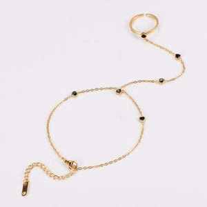 Detailed view of a gold-tone finger bracelet with black heart charms and adjustable chain